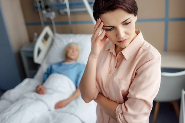 Selective focus of sad daughter with sick mother in bed on background in hospital — Stock Photo