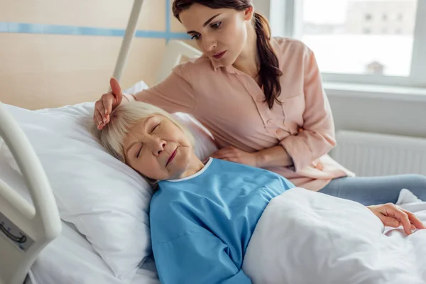 Стурбована дочка сидить на ліжку біля сплячої старшої матері в лікарні — стокове фото