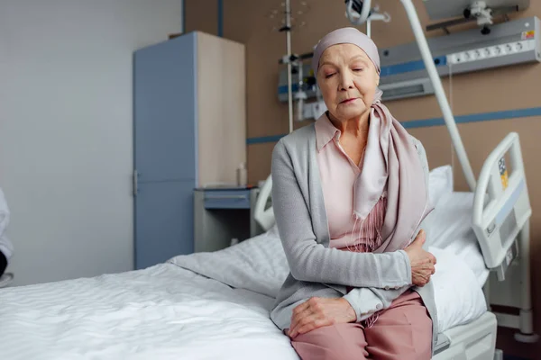 Femme âgée avec cancer assis sur le lit à l'hôpital avec les mains croisées — Photo de stock