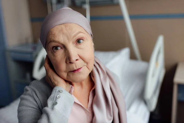 Turbato donna anziana con il cancro seduto sul letto in ospedale e guardando la fotocamera — Foto stock