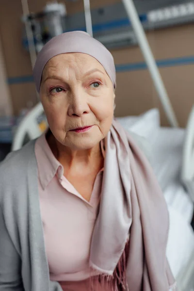 Sad senior woman with cancer sitting on bed in hospital and looking away — Stock Photo