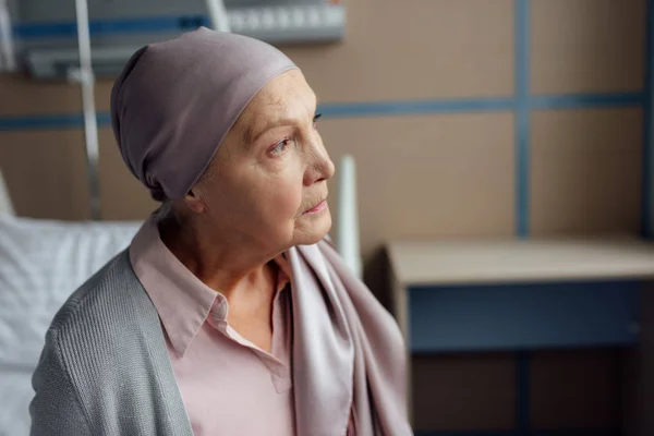 Грустная пожилая женщина с раком сидит на кровати в больнице — стоковое фото