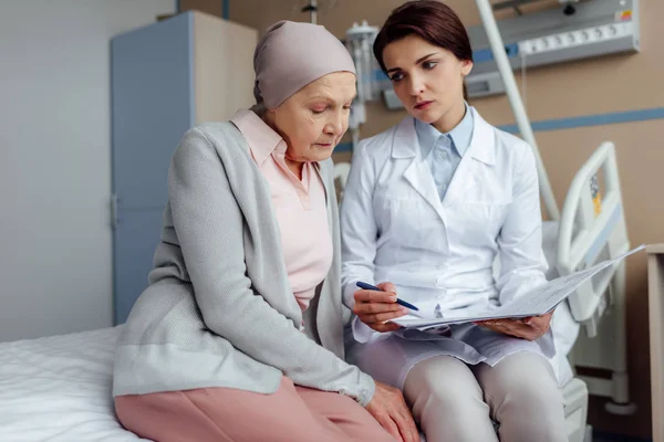 Upset female doctor holding diagnosis and consulting senior woman with cancer in hospital — Stock Photo