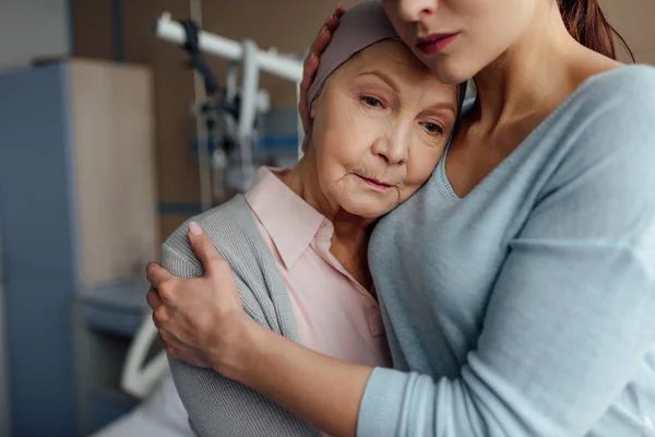 Concentrazione selettiva della figlia che abbraccia la madre anziana malata con il cancro in ospedale — Foto stock