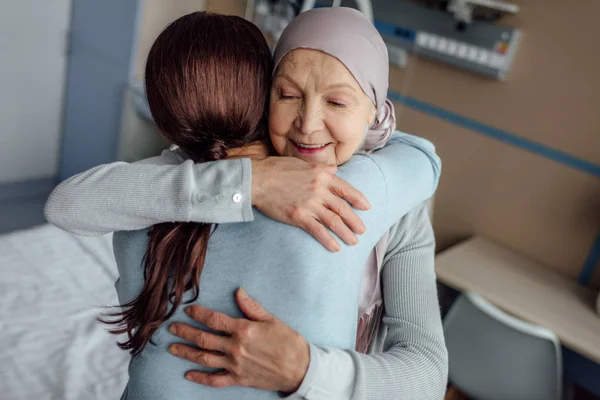 Femme âgée souriante dans un mouchoir embrassant sa fille à l'hôpital — Photo de stock