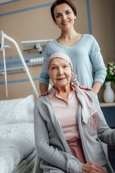 Donna anziana sorridente in fazzoletto con figlia che guarda la macchina fotografica in ospedale — Foto stock