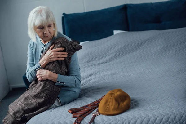 Verärgerte Seniorin sitzt auf Bett und hält Jacke zu Hause — Stockfoto