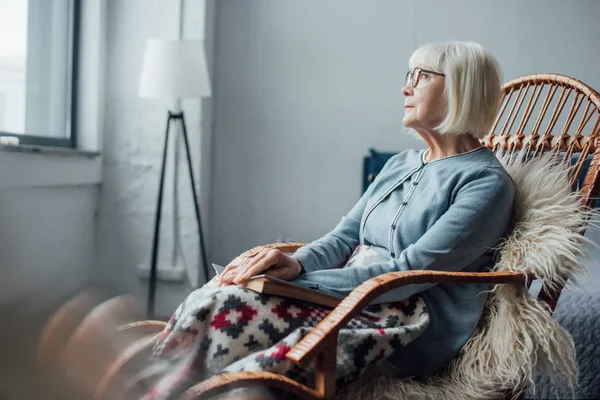 Selektiver Fokus der Seniorin, die mit Buch zu Hause im Wickelstuhl sitzt — Stockfoto
