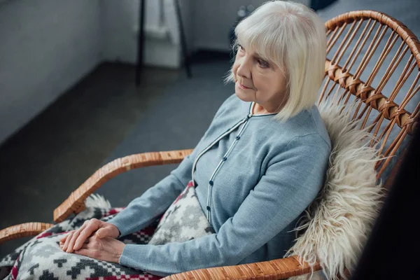 Triste femme âgée assise dans un fauteuil berçant en osier à la maison — Photo de stock