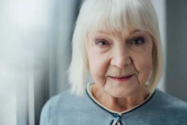 Portrait d'une femme âgée souriante aux cheveux gris regardant la caméra à la maison — Photo de stock