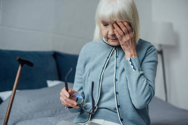 Грустная пожилая женщина в очках и седых волосах вытирающая слезы и плачущая дома — стоковое фото