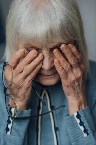 Portrait of senior woman with glasses and grey hair wiping tears and crying at home — Stock Photo