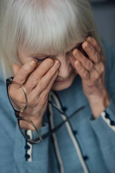 Selektiver Fokus einer Seniorin mit Brille und grauem Haar, die zu Hause Tränen wischt und weint — Stockfoto