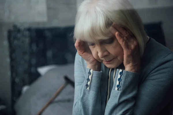Selektiver Fokus einer Seniorin mit Händen auf dem Kopf, die zu Hause Kopfschmerzen hat — Stockfoto