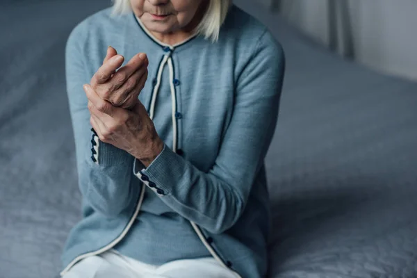 Partial view of senior woman sitting on bed and measuring pulse with hand at home — Stock Photo