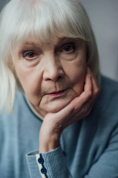 Porträt einer traurigen Seniorin, die ihr Kinn mit der Hand stützt und in die Kamera blickt — Stockfoto