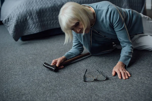 Lonely senior woman lying on floor with walking stick and feeling unwell at home — Stock Photo