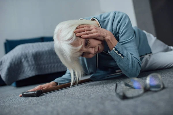 Solitaria mujer mayor acostada en el suelo y con dolor de cabeza en casa - foto de stock