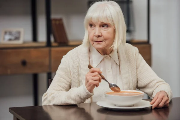 Einsame Seniorin sitzt am Tisch und isst zu Hause Sahnesuppe — Stockfoto