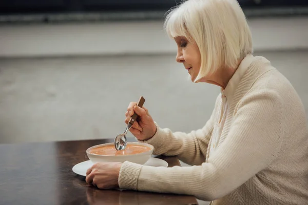 Triste mulher sênior sentado à mesa e comer sopa de creme em casa — Fotografia de Stock