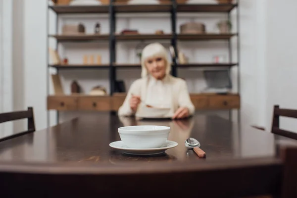 Enfoque selectivo de tazón y cuchara en la mesa con la mujer mayor en el fondo - foto de stock