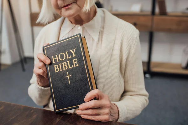 Cropped view of senior woman holding holy bible at home — Stock Photo