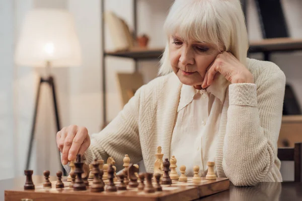 Nachdenkliche Seniorin sitzt am Tisch und spielt zu Hause Schach — Stock Photo