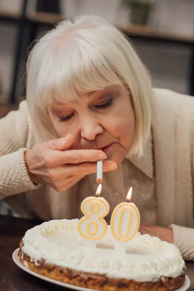 Mulher sênior acendendo cigarro de velas acesas no bolo de aniversário em casa — Fotografia de Stock