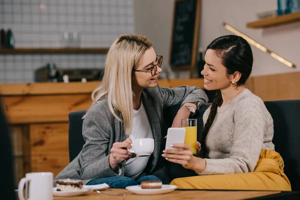 Femmes souriantes bavardant tout en tenant des boissons dans le café — Photo de stock