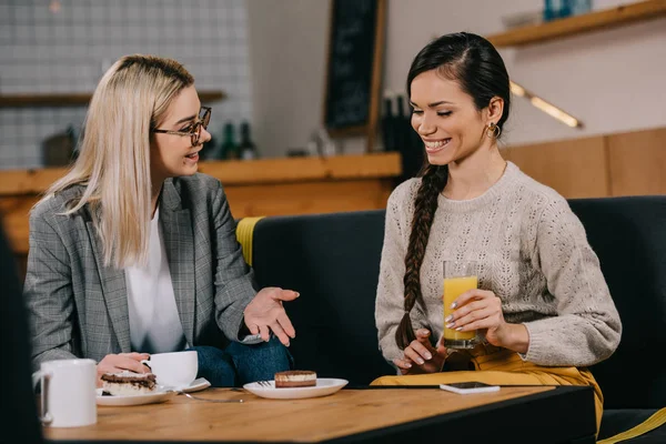 Улыбающаяся женщина болтает с другом, держа напиток в кафе — стоковое фото
