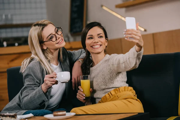 Mujeres alegres sonriendo mientras toma selfie en la cafetería - foto de stock