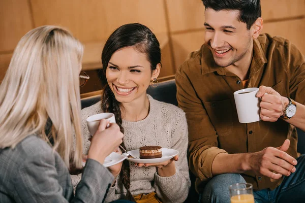 Mujer alegre charlando con amigos mientras sostiene el pastel en la cafetería - foto de stock