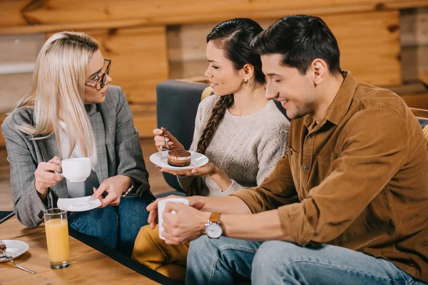Mujer sonriente charlando con amigos mientras sostiene la torta en la cafetería - foto de stock