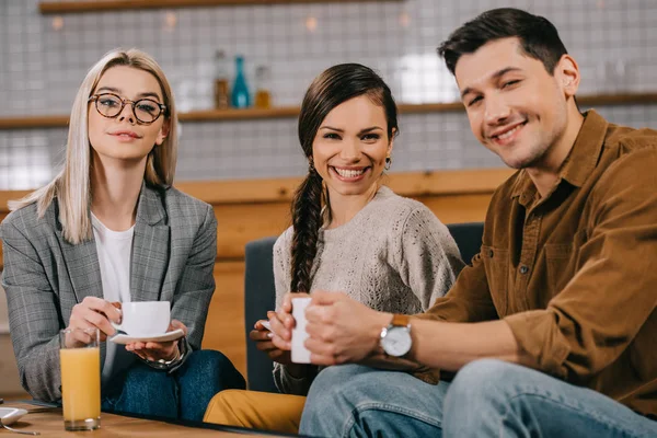 Grupo sonriente de amigos sosteniendo tazas en la cafetería - foto de stock