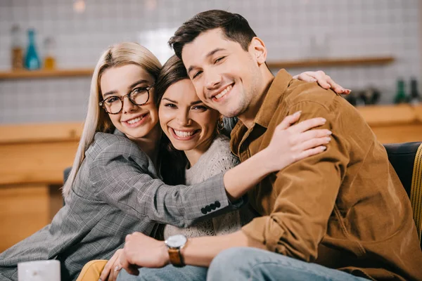 Mujer sonriente en gafas abrazando amigos en la cafetería - foto de stock