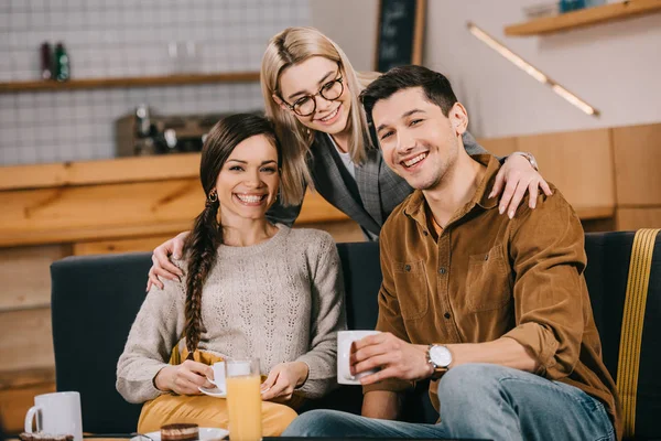 Mulher feliz em óculos abraçando amigos no café — Fotografia de Stock