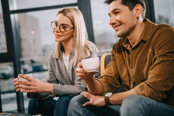 Alegre pareja sosteniendo tazas con bebidas - foto de stock