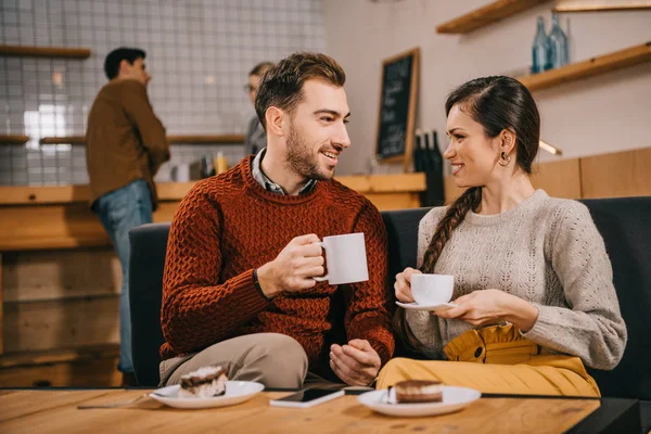 Selective focus of couple holding cups and chatting in cafe — Stock Photo