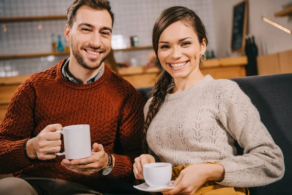 Couple holding cups and smiling in cafe — Stock Photo