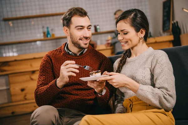 Hombre feliz mirando a la mujer atractiva con pastel en la cafetería - foto de stock