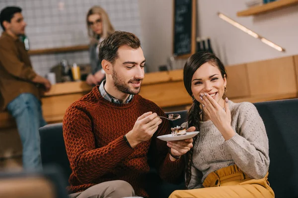 Hombre guapo sentado con mujer atractiva y la celebración de la torta en la cafetería - foto de stock