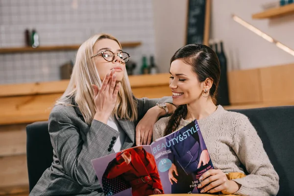 Atractiva mujer mirando a su amigo mientras sostiene la revista de belleza - foto de stock
