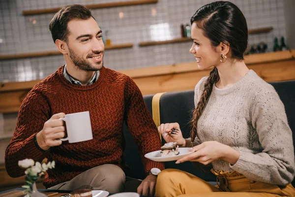 Atractiva mujer mirando a novio mientras sostiene pastel en la cafetería - foto de stock