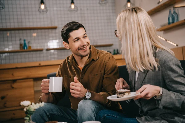 Sonriente hombre mirando a novia con pastel en la cafetería - foto de stock