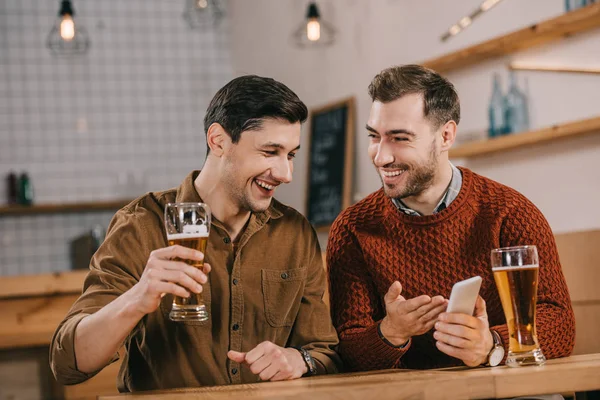 Alegres hombres guapos sonriendo mientras mira el teléfono inteligente - foto de stock