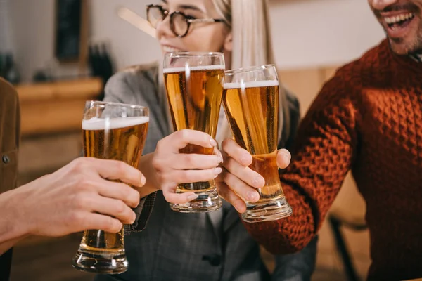 Cropped view of happy woman clinking with beer with friends — Stock Photo