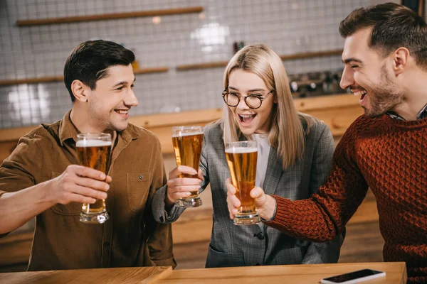 Atractiva mujer sosteniendo vidrio con cerveza cerca de amigos masculinos - foto de stock