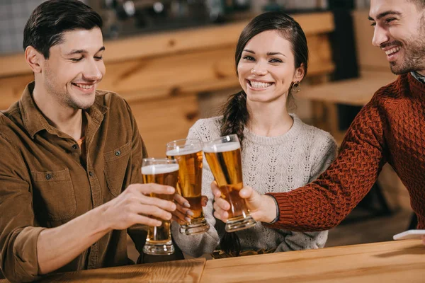 Mulher feliz sorrindo perto de amigos enquanto clica com cerveja — Fotografia de Stock