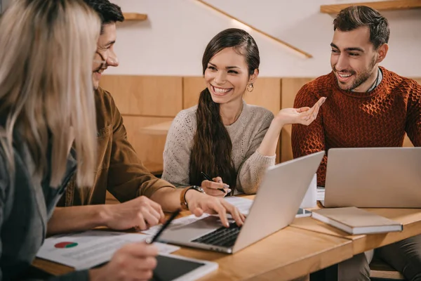 Cheerful group of coworkers talking in cafe near laptops — Stock Photo