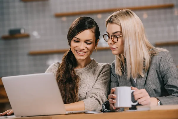 Amigas mirando el portátil en la cafetería - foto de stock